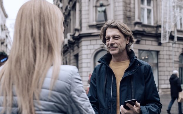 Gesprächssituation Mann auf Straße, ca. 40 Jahre, erklärt einer Frau mit blonden langen Haaren (Rückenansicht) etwas.